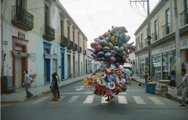 En el cruce de una calle, apenas podemos ver la cabeza y pies de un hombre por entre una multitud de globos y juguetes inflables.