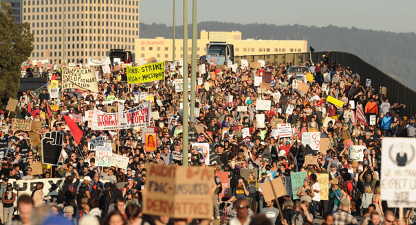 Multitudes de manifestantes convergen en el Puerto de Oakland. Muchos portan letreros y banderas.