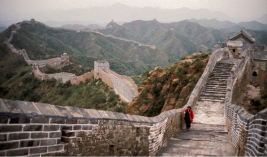 Fotografía a color de una persona caminando en sentido ascendente sobre la Gran Muralla China.