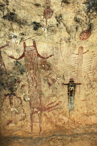 A 10-foot-tall anthropomorph in Panther Cave with upraised arms, U-shaped head, and a feather hip-cluster-like adornment on its left side. An atlatl loaded with a dart is portrayed in the figure's right hand, and in its left hand are additional darts as well as other paraphernalia.