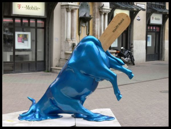 Frente a una tienda de telefonía móvil está la estatua de una vaca azul brillante de cuyo trasero sale un palito de paleta helada y, tal como una paleta helada, se está derritiendo.