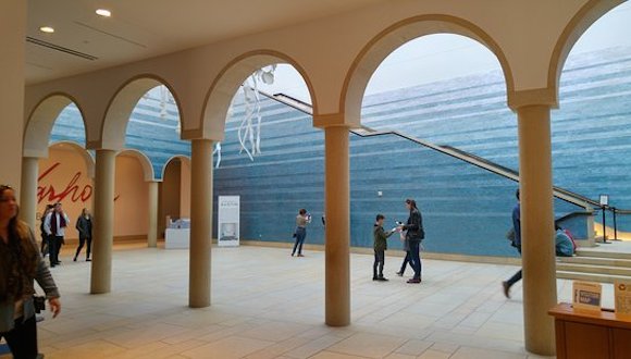 An inner colonnade at the Blanton Museum, featuring arches, columns, and a blue wall in the background that is an art installation.  