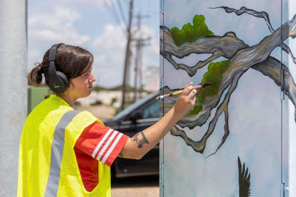 An artist commissioned by Up Art Studio paints a mini-mural on a traffic control box.