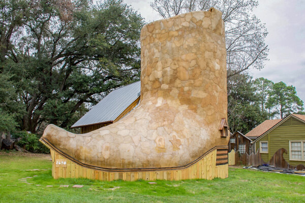 A photograph of a house built in the shape of an oversized boot. The house was built from reclaimed or recycled materials by Dan Phillips.