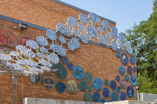 Photograph of the outside of the brick Lowman Student Center at Sam Houston State University. The image depicts a mural designed by artist Dan Phillips. The mural is made of small connected circles that form a twisted ladder design.