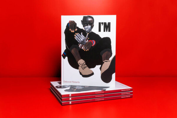 A stack of books sitting on a red table and against a red background. One book is standing up, and features the word "I'm" and a figure made up of different collaged elements.