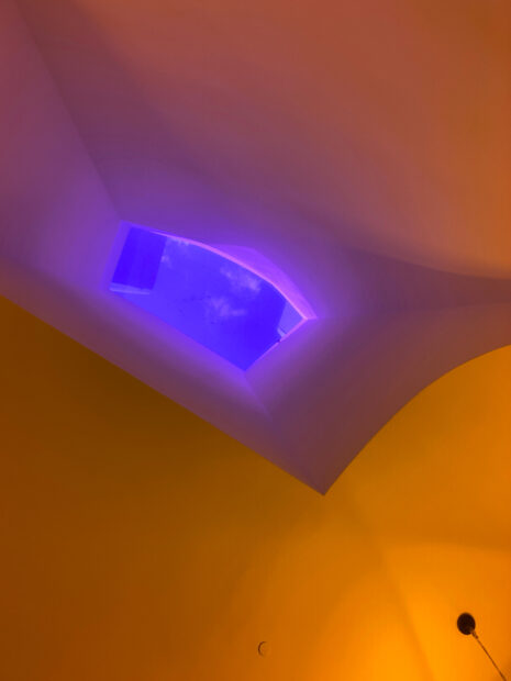 A photograph of a skylight that interrupts the bright yellow lighting inside a tunnel walkway. Installation by Ólafur Elíasson.