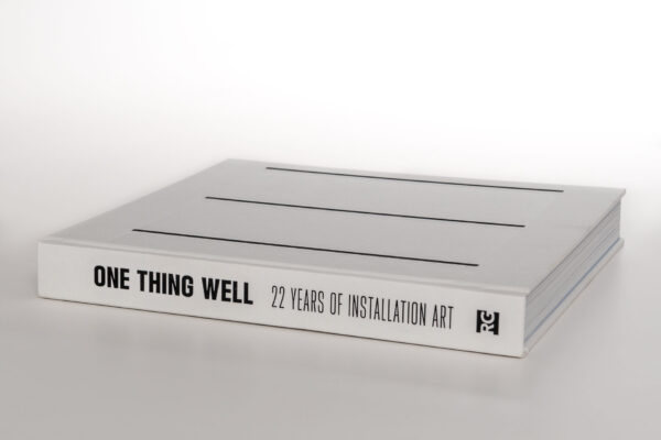 Photograph of the book One Thing Well: 22 Years of Installation Art. The book is white, with black text
