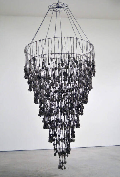 A chandelier-shaped hanging sculpture by Houston artist Joe Mancuso. The piece is black and is made out of steel, roses, and concrete. 