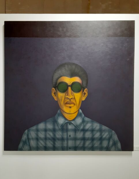 A portrait of a person wearing sunglasses and a plaid shirt. The person is looking stright out of the canvas.