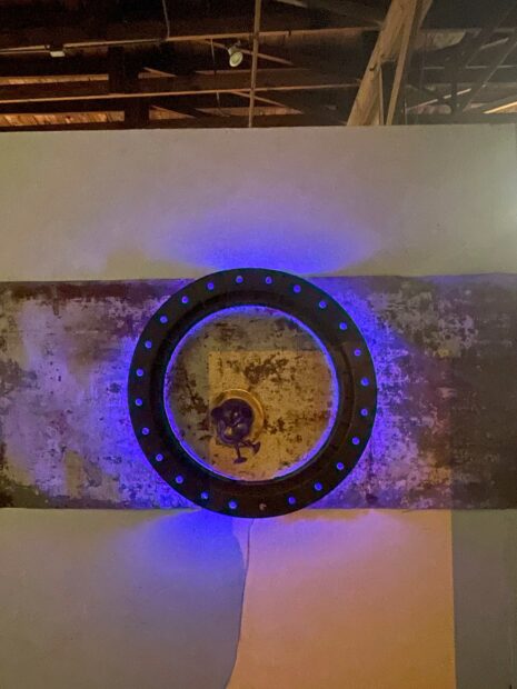 A sculpture by artist Brian Wedgworth. The piece features blue-purple LEDs around a center ring, which is hung on a wall.