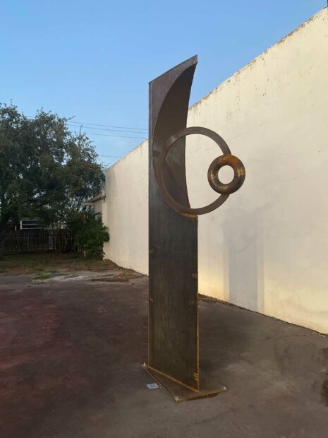 A metal sculpture by artist Brian Wedgworth. The sculpture consists of a vertical component, with two smaller, hollow circle components attached to it.