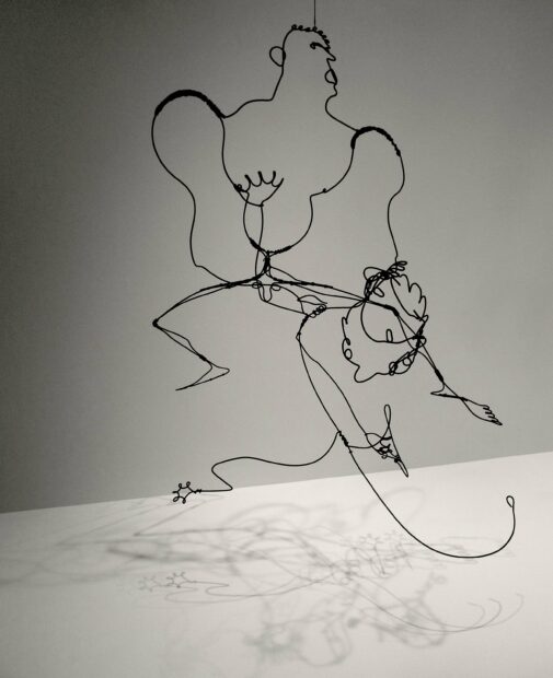 A hanging mobile and sculpture by Alexander Calder. A wire piece with a figure suspended over a white base