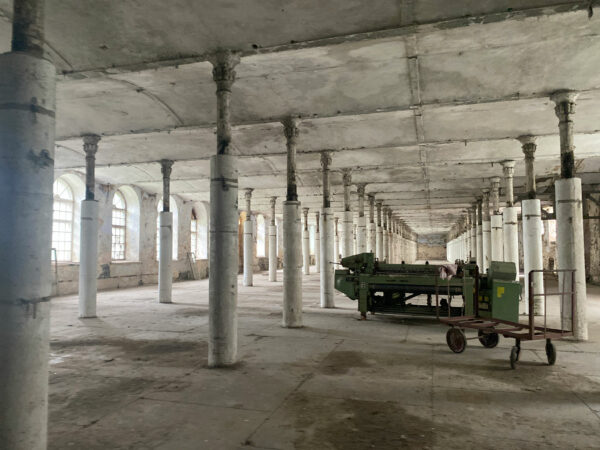 The interior of an abandoned factory. It is an empty, concrete space featuring many columns.