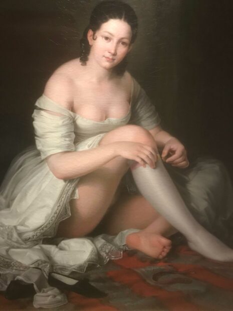 Painting of a woman who is sitting down, removing her garter. She is wearing a white, low-cut dress