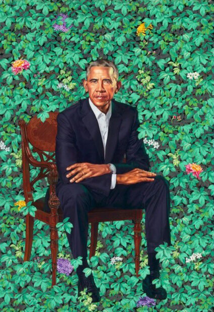 A realistic painting of President Barack Obama. He wears a suit and sits in a chair with his arms crossed resting on his knees. The background is filled with leaves like an ivy wall and various flowers are interspersed among the leaves. Portrait by Kehinde Wiley