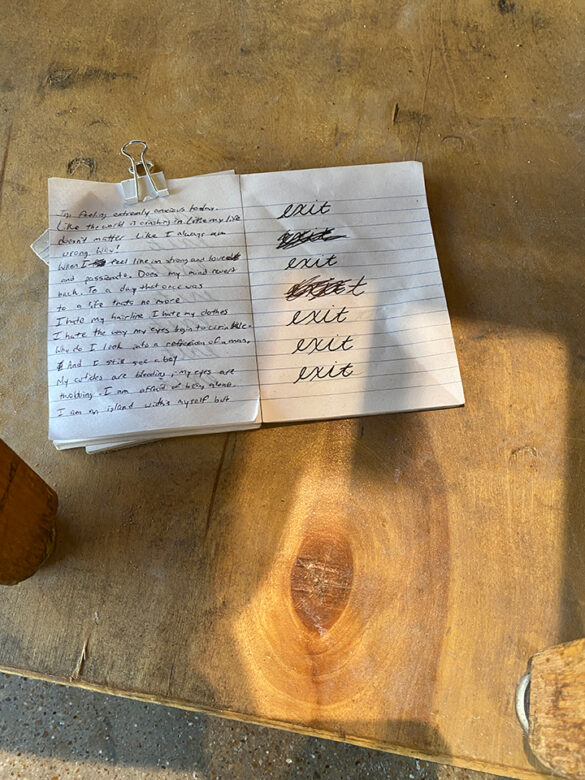A close-up photograph of a small notebook that sits on a dolly in an installation by Benjamin Loftis. The notebook has hand written text and is a first person narrative discussing the artist's issues with body image.