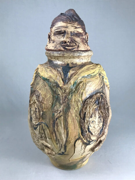 A photograph of a sculpture of a figure. The body of the figure has two images of people carved into the sides. Artwork by Earnest Snell.