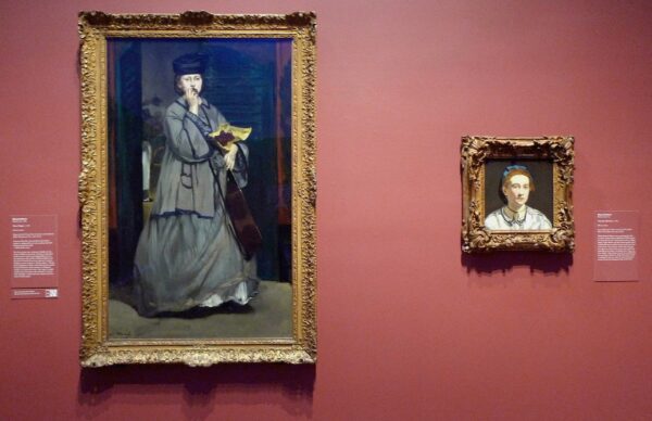 Installation view of a portrait of a woman and a full figure against a pink wall