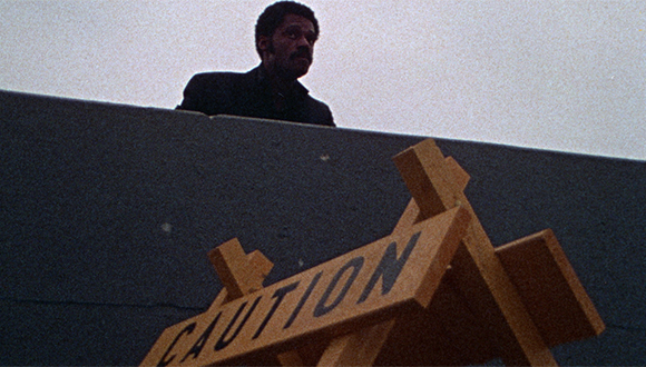 Film still showing a man looking over a caution sign