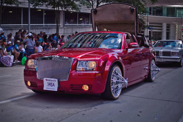 A glossy red convertible with elbow wheels, known as swangas, participates in the Houston Art Car Parade. 