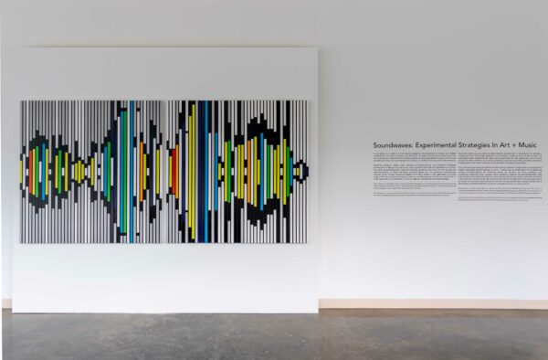 Image of a multicolored sound graph with the title wall and exhibition text on the right.