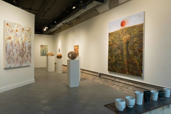 An installation view of the exhibition A Commitment to What is Before you at Northern-Southern Gallery in Austin. A view of the work of all three artists in the exhibition including, ceramic cups, sculptures made from traditional basket weaving techniques on pedestals in the center, and paintings in both large and small scale on the walls surrounding.