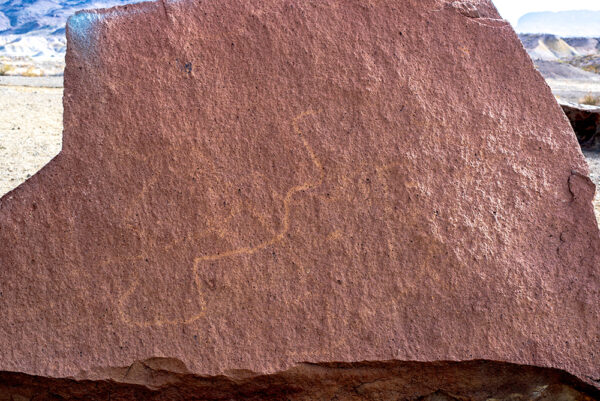 A photograph of a red stone with a lightly etched organic-shaped petroglyph. Photo by Paul Leicht.