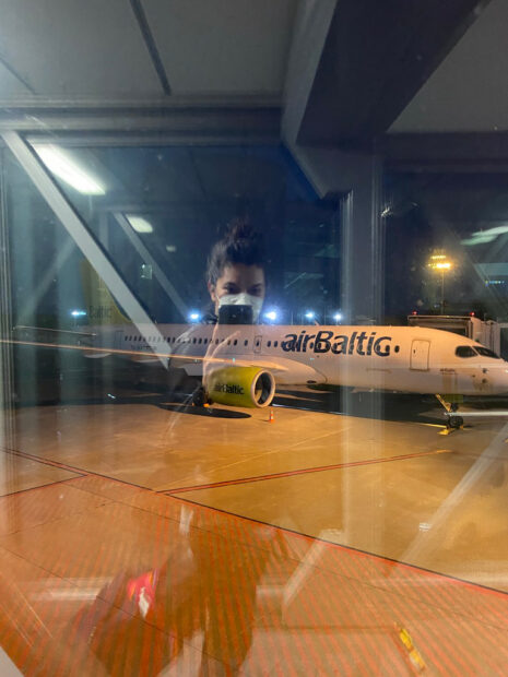 Photograph of an air baltic airplane. The photo is taken out of a window and you can see the photographer's reflection in the glass