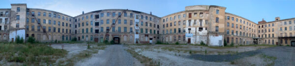 A panorama photograph of a factory building. The building is in disrepair, and is four stories tall.
