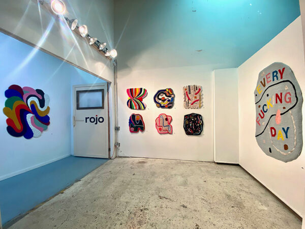 A photograph of the interior of a gallery with brightly colored fiber works on the walls.