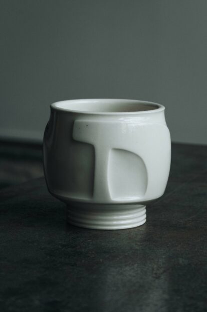 A small porcelain cup by artist Ryan McKerley. A small sculpture with carved details and a narrow base.