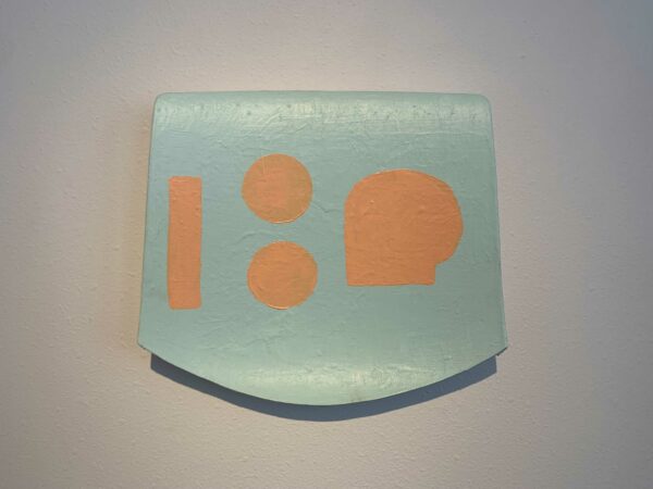 A rectangular form painted turquoise. The bottom of the form is rounded, and there are shapes — circles, a rectangle, and an organic shape — on the surface of the object.