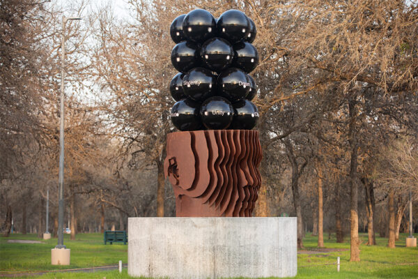 A photograph of a new public art work by Kaldric Dow. The sculpture is of an anonymous head topped with four columns of four rows of black reflective spheres.