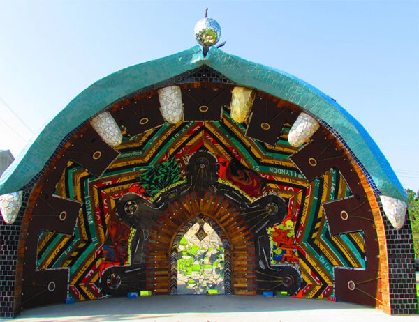 A photograph of an amphitheater stage with a brightly colored mosaic-style arch shaped backdrop. 