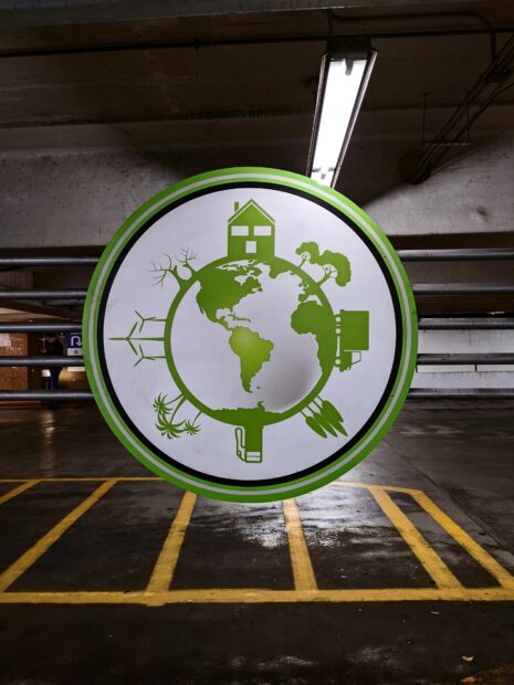 A photograph of the interior of a parking garage. The center of the photo has a large, circular object, on which there is the image of the Earth, along with houses, trees, cars, palm trees, and wind turbines.