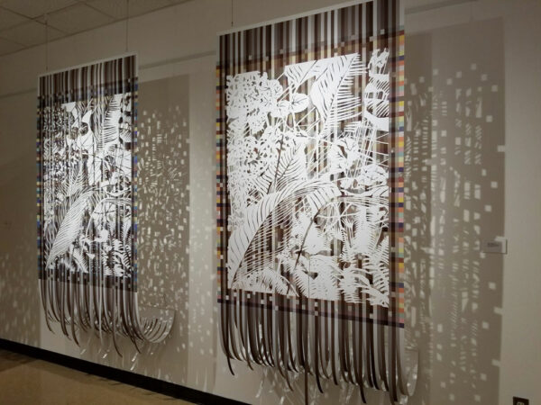 An installation image showing large two cut paper hanging works by Sangmi Yoo. Each work has a colorful pixelated background with a detailed white cut paper image depicting leaves. 