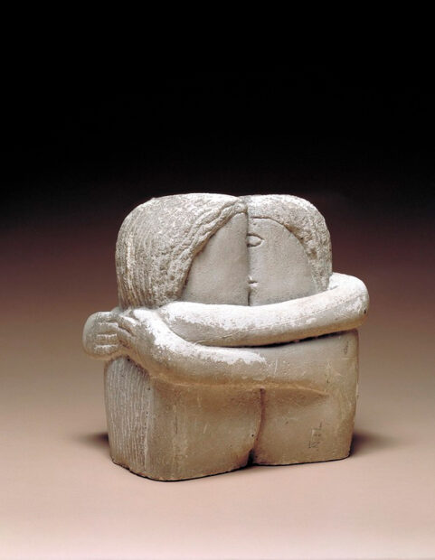 A plaster sculpture of two figures embracing, hugging, and kissing.