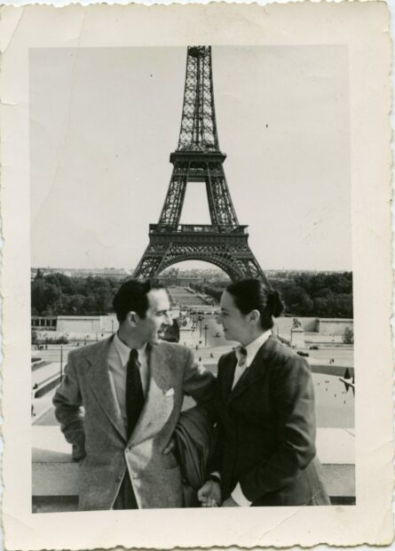 A black and white photograph dated around 1950 of Carmen Herrera and her husband Jesse Loewenthal in Paris with the Eiffel Tower behind them in the distance. The couple looks directly at each other rather than the camera.