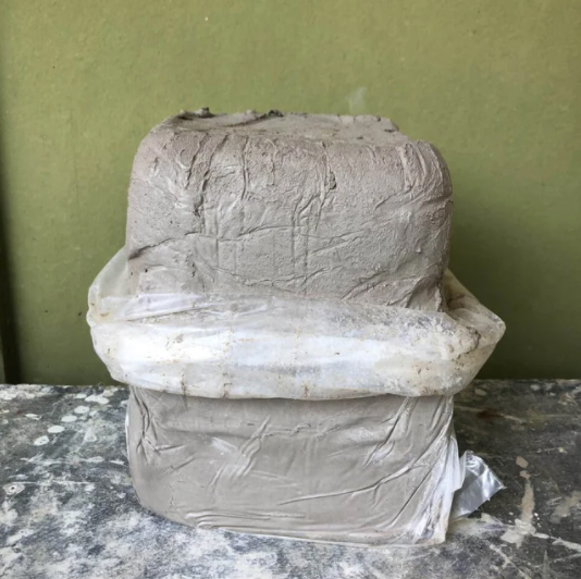 A block of gray clay, sitting on a table in a bag.