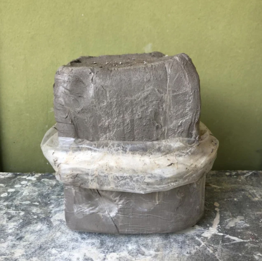 A block of gray clay, sitting on a table in a bag.