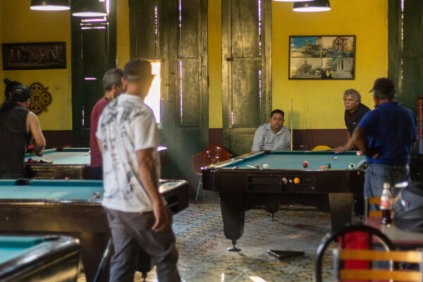 Dentro de un club de billar, varios grupos de hombres juegan pool en diferentes mesas en El Salvador
