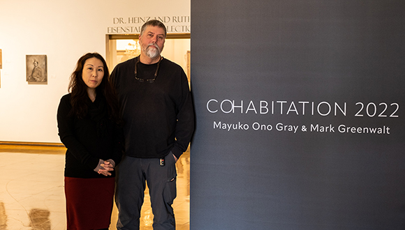 Portrait of the artist couple next to the title wall of their exhibition