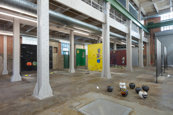 Installation view of large paintings standing in armatures with vases on the floor