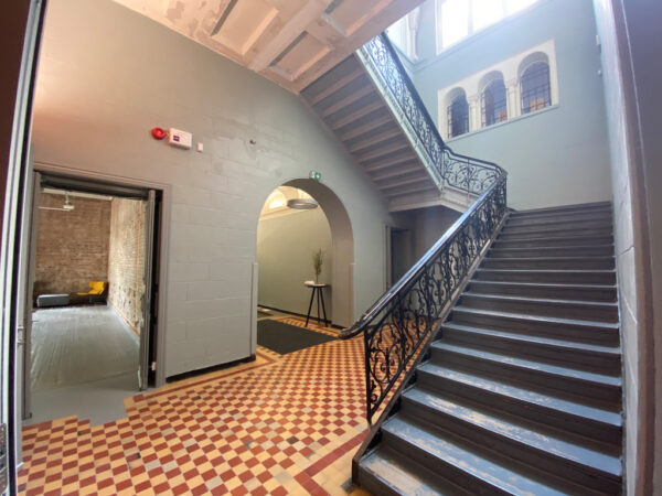 Interior view of the main stairwell of the Narva Artist Residence. The photo shows a wrought iron banister with a stairwell that swoops up and around the large space.