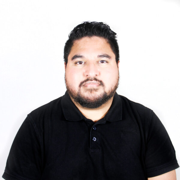 A headshot of Isabel Servantez. He wears a black button-up short sleeve shirt and looks directly at the camera. 