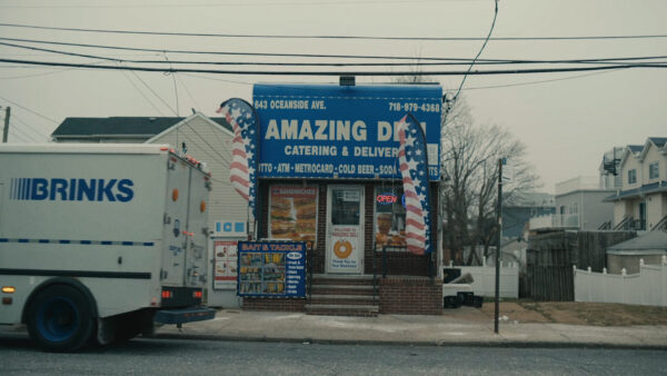 Still image from a film that shows a Brinks Security truck in front of a traditional New York City style Bodega