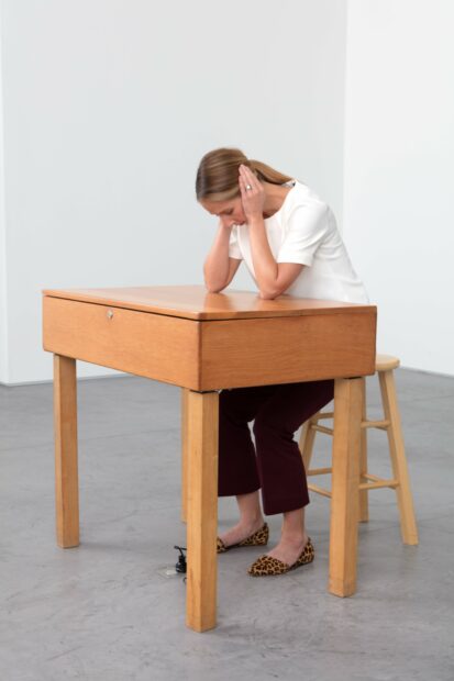 Photo of a woman sitting at a desk with her hands cupped over her ears listening to a sound piece