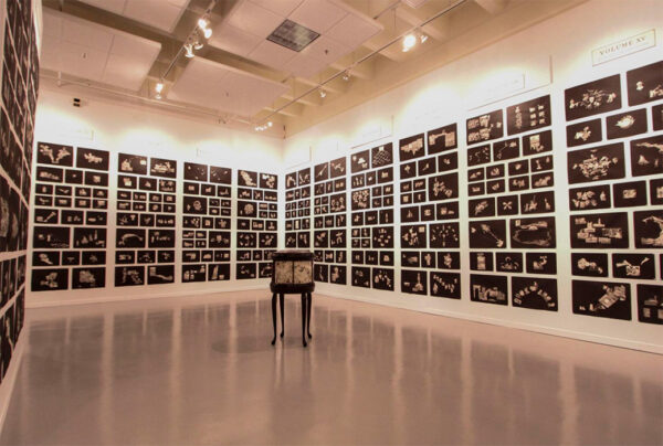 An installation image of collages by Mel Chin filling the walls of a gallery.