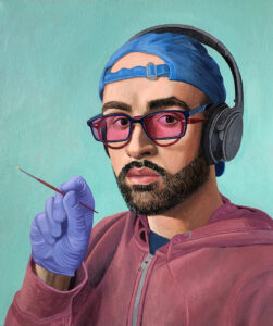 A self-portrait of Francisco Moreno.  The performer wears a blue backwards baseball cap with a pair of black wireless headphones on it.  He wears navy blue framed glasses with pink lenses over a pair of brown framed glasses.  He has a short beard and looks straight at the viewer.  He wears a navy blue shirt under a purple hoodie.  A hand is raised revealing a blue latex glove holding a small fine brown paintbrush.  The artist is placed on a light teal blue background.